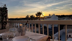 Een eettafel op een balkon met uitzicht op een zonsondergang.