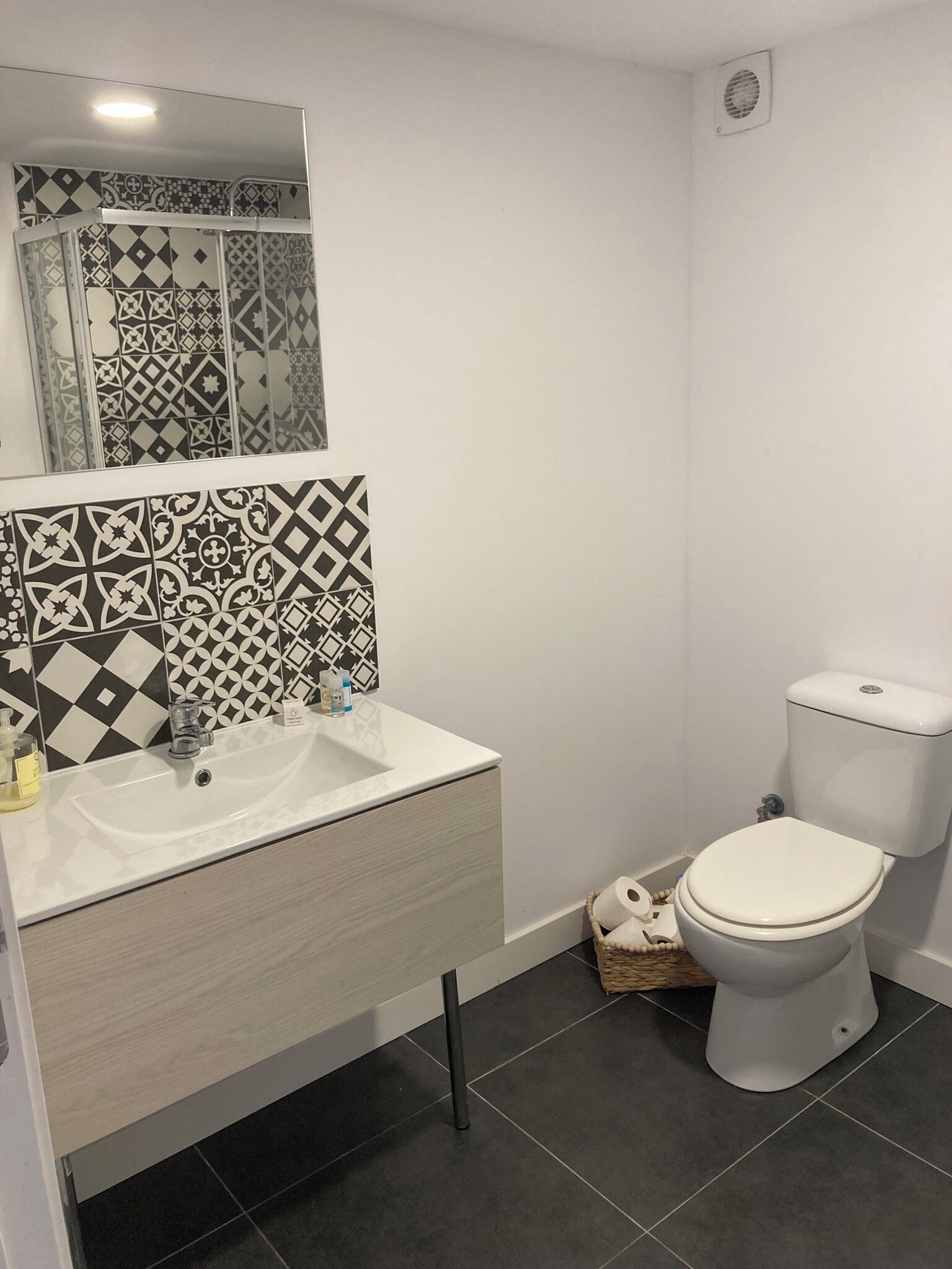 A bathroom with a white sink, black and white patterned tiles, a toilet, and a mirror above the sink.
