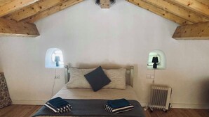 Een slaapkamer met een schuine plafond, een bed met een beddegoed met dessin, twee bedlampen en een radiator.