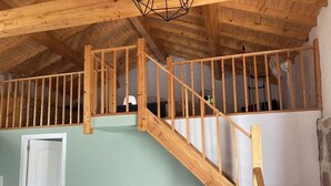 Een slaapkamer in een loft met een houten trap, een bed en een bureau met een stoel.