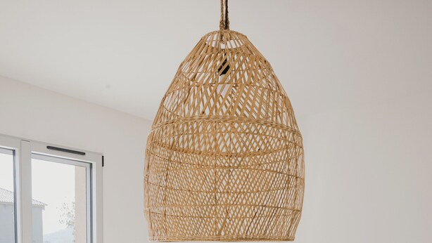 Ein Schlafzimmer mit einem großen Bett, einem Holz-Kopfteil, einer Hängeleuchte aus Weidwerk und Blick durch eine Glastür.