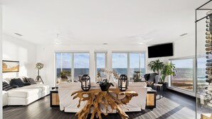 Ein modernes Wohnzimmer mit einem großen Holztisch, weißen Sofas und Blick auf den Ozean.