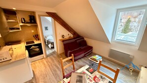 A compact living space with a kitchen, a dining area, and a sleeping area. There is a loft bed with a view of the outside.