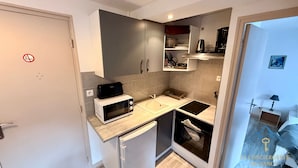 A compact kitchen with a microwave, sink, and stove. There is a door with a no-smoking sign.