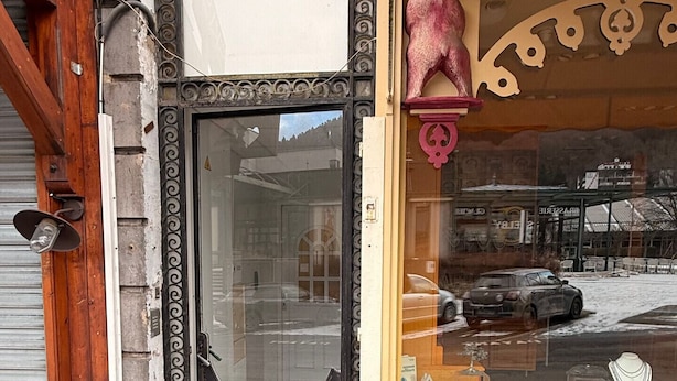 A storefront with a closed metal shutter, a wooden door frame, and a glass window displaying jewelry.
