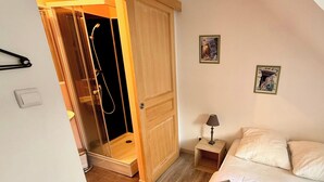 A bedroom with a wooden wardrobe, a bed with white bedding, a nightstand with a lamp, and two framed pictures on the wall.