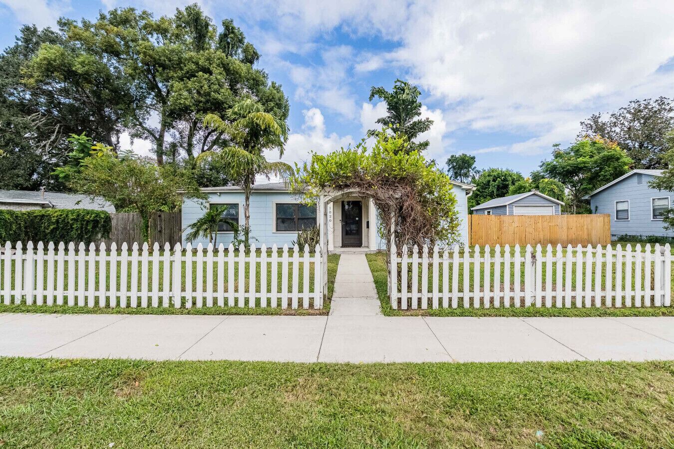A residential area with a house featuring a front porch, a white picket fence, and a well-maintained lawn.