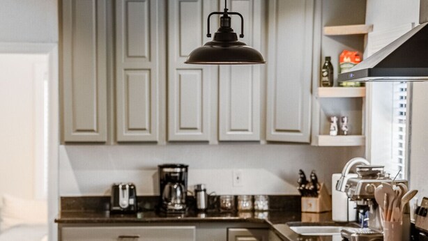 Cozinha moderna com armários cinza claro, luminária pendente preta, cafeteira e ilha integrada com banquetas.
