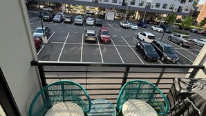 A balcony with green chairs and a table, overlooking a parking lot and a multi-story building. - 1 bedroom with access to living & kitchen in adorable East Orange with AC & gym. (East Orange)