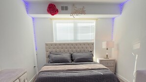 A bedroom with a bed, a dresser, a nightstand, and a window with blinds. - 1 bedroom with access to living & kitchen in adorable East Orange with AC & gym. (East Orange)