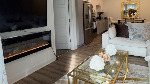 A modern living room with a flat-screen TV, a fireplace, a white sofa, and a glass coffee table. - 1 bedroom with access to living & kitchen in adorable East Orange with AC & gym. (East Orange)
