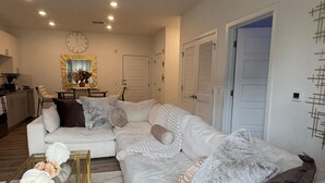 A modern living room with a white sofa, a glass coffee table, and a decorative mirror. - 1 bedroom with access to living & kitchen in adorable East Orange with AC & gym. (East Orange)