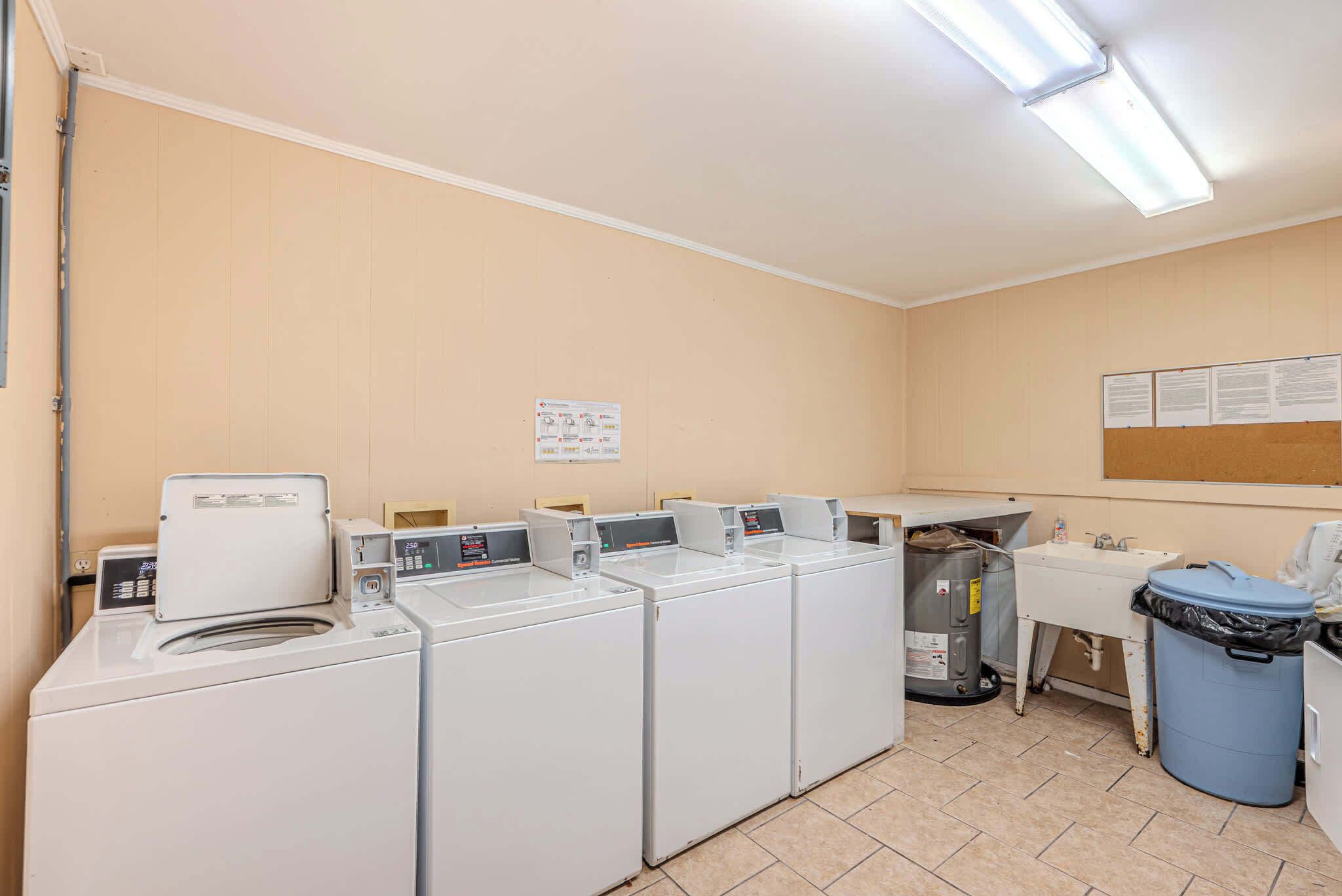 Un cuarto de lavandería con varias lavadoras, un lavabo y un cubo de basura.