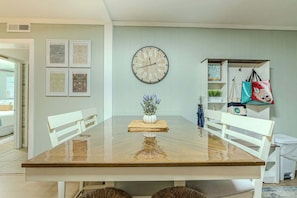 Un coin repas avec une table en bois, des chaises blanches, une horloge murale et des citations inspirantes encadrées.