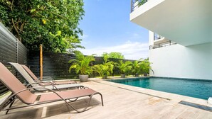 Un área junto a la piscina con sillones de descanso, una piscina y plantas en macetas.