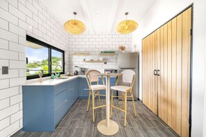 Eine moderne Küche mit weißen und blauen Schränken, einer zentralen Kochinsel mit zwei Stühlen, einem Kühlschrank und einer Holztür.
