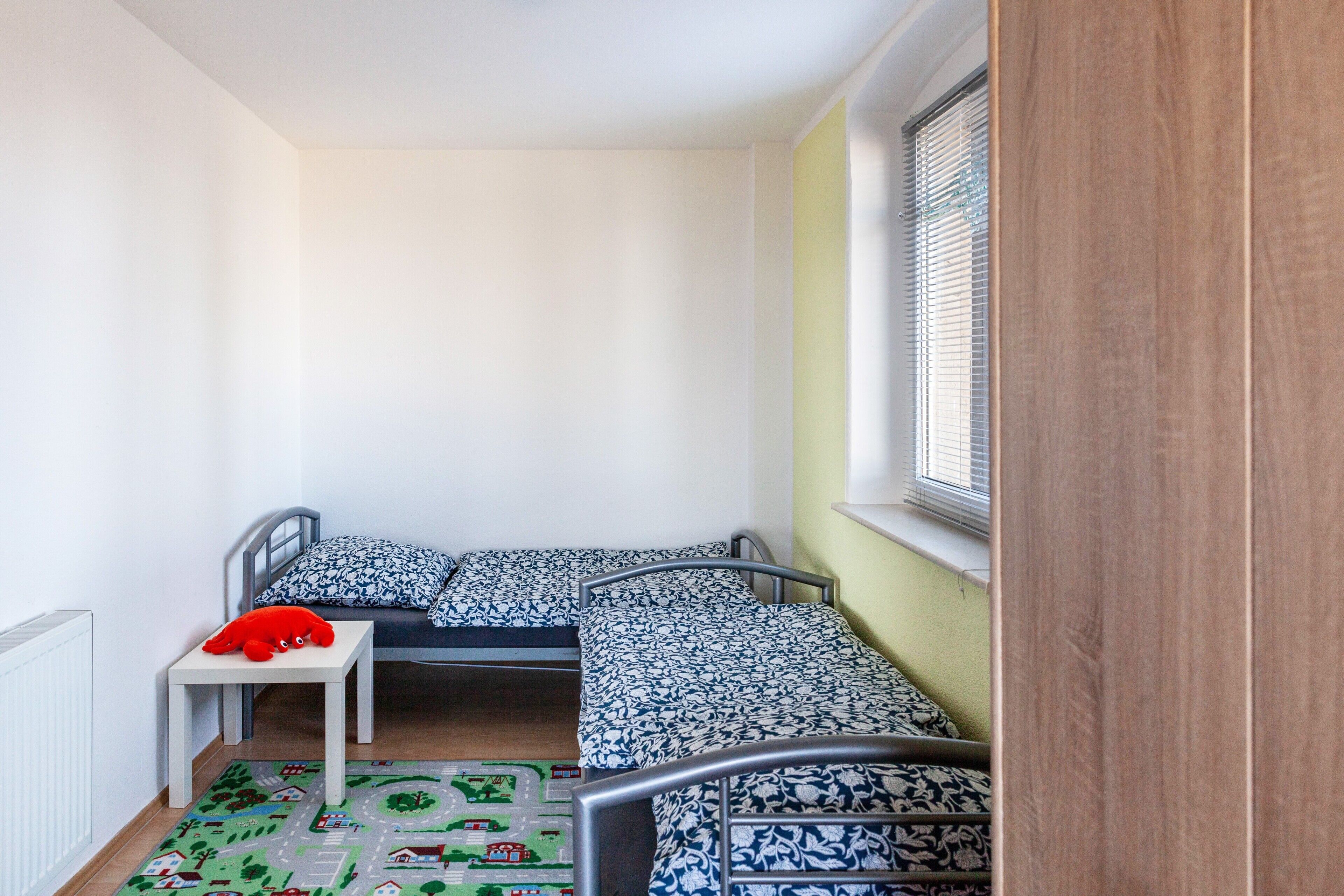 Ein Kinderzimmer mit einem Etagenbett, einem kleinen Tisch mit einem roten Spielzeug und einer Spielmatte auf dem Boden.
