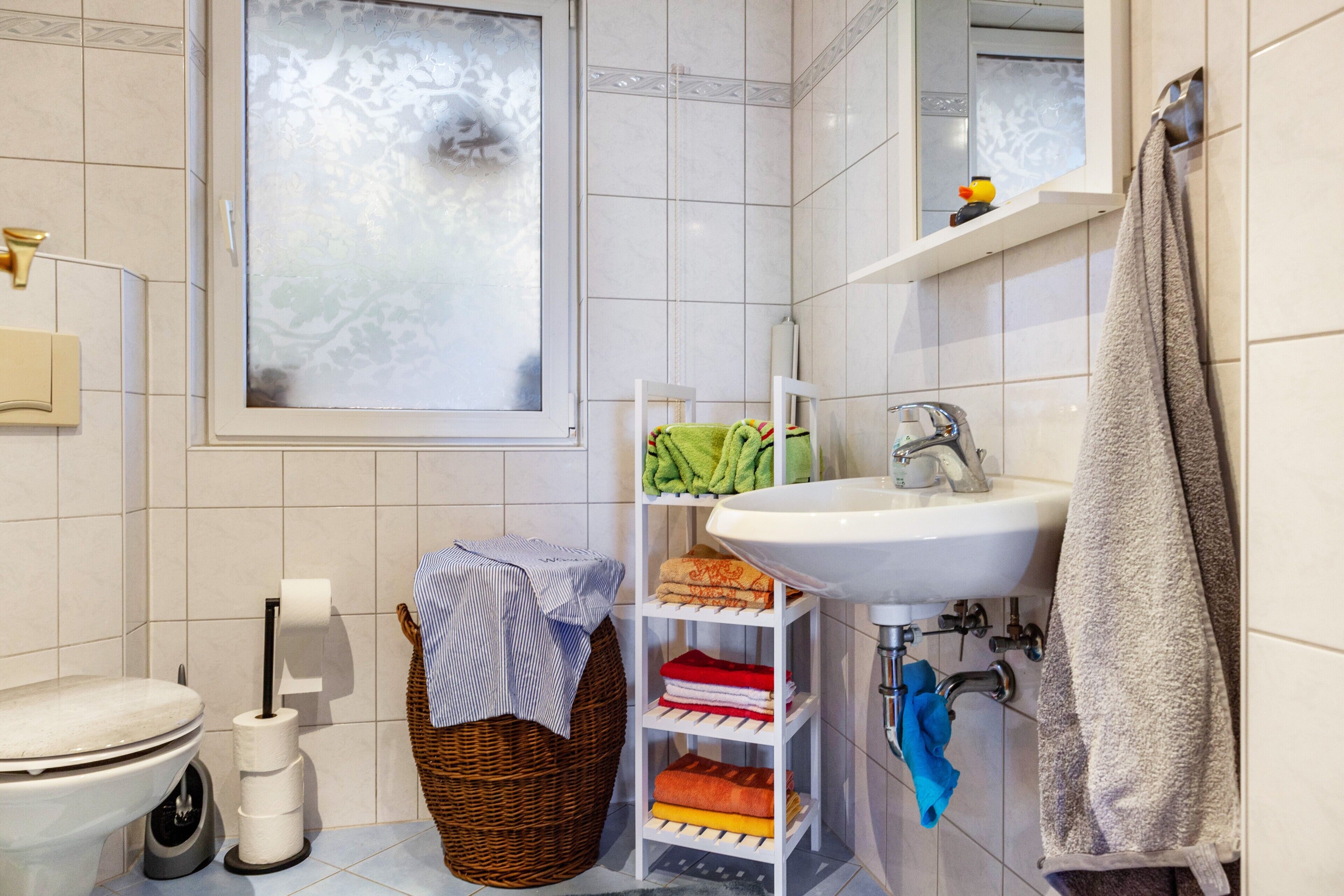Un baño con inodoro, lavamanos, ventana, toallero y estante con toallas.
