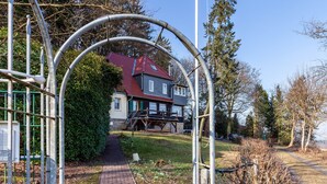 A pathway leading to a house with a red roof, surrounded by trees and a metal structure.