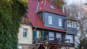 A two-story house with a red roof, a balcony, and a stone foundation.