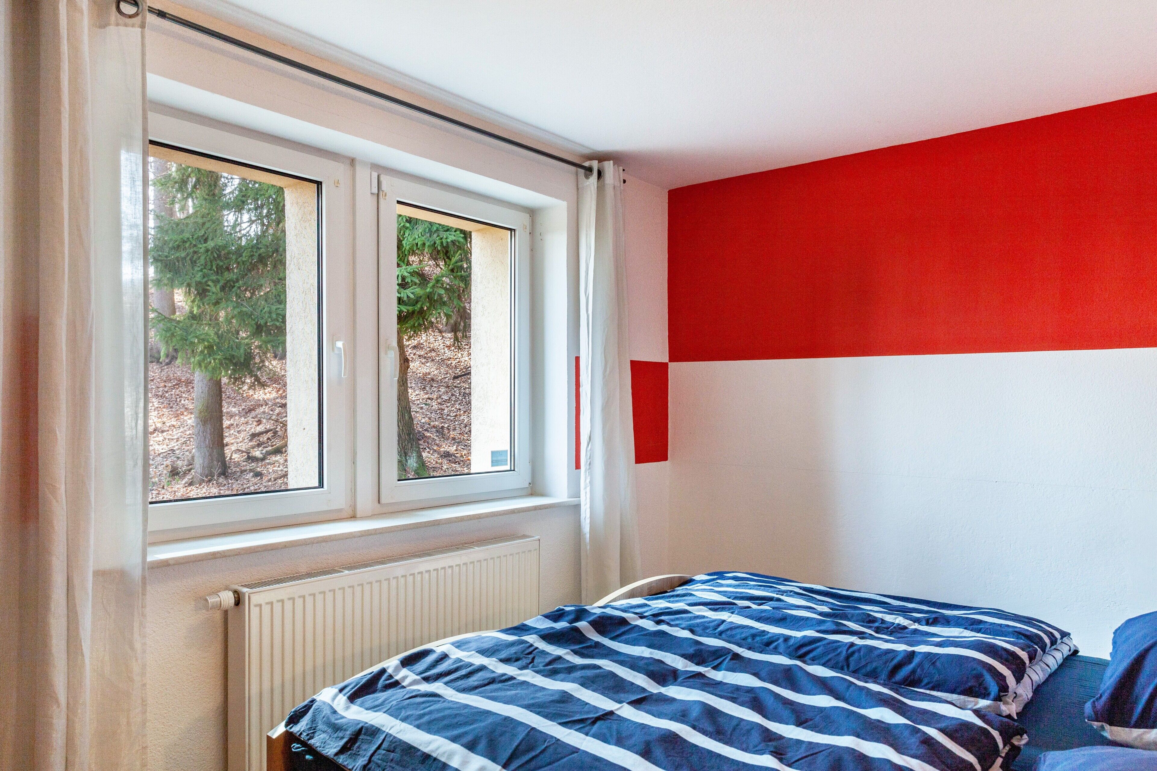 A bedroom with a bed, a window, and a red wall.