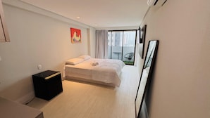 A modern bedroom with a large bed, a small black nightstand, a painting on the wall, and a view of the outside balcony. - Flat Aconchegante em João Pessoa (João Pessoa)