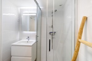 Ein Badezimmer mit einer gläsernen Duschkabine, einem weißen Waschbecken und einem hölzernen Handtuchhalter.