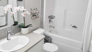 A modern bathroom with a shower, toilet, and sink, featuring a mirror, potted plants, and a towel rack. - Mahogany Escape - Your Calgary Oasis (Calgary)
