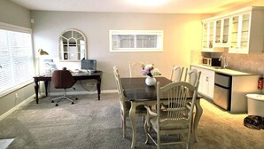A dining area with a table and chairs, a computer desk with a chair, a window with blinds, and a kitchen area with cabinets and appliances. - Mahogany Escape - Your Calgary Oasis (Calgary)