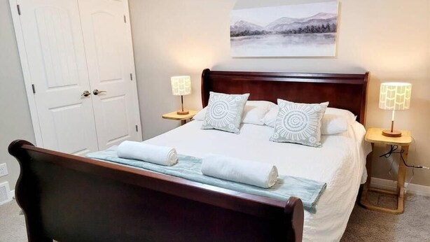 A neatly made bed with a wooden headboard, two bedside lamps, and a framed picture on the wall. - Mahogany Escape - Your Calgary Oasis (Calgary)