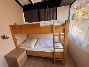 Ein Stockbett mit einer Leiter, eine hölzerne Kommode und ein Fenster mit Vorhängen.