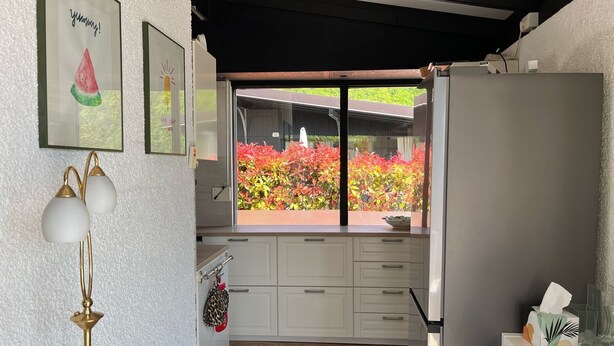 A kitchen with white cabinets, a refrigerator, and a window with a view of colorful plants. - Vacation bungalow with a wonderful view of Lake Garda and Monte Baldo (Tignale)