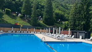 A swimming pool with lounge chairs and umbrellas, surrounded by a wooden fence and trees. - Vacation bungalow with a wonderful view of Lake Garda and Monte Baldo (Tignale)