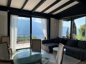 Un salon moderne avec une table en verre, des canapés sombres et de grandes fenêtres donnant sur une vue imprenable sur les montagnes.