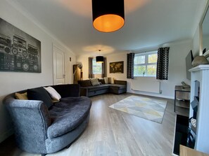Een moderne woonkamer met een gebogen grijze bank, een wereldkaart aan de muur en een groot raam met patroon gordijnen.