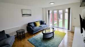 Ein modernes Wohnzimmer mit einem grauen Sofa, einem runden Couchtisch und einer großen Glasschiebetür, die in einen Garten führt.