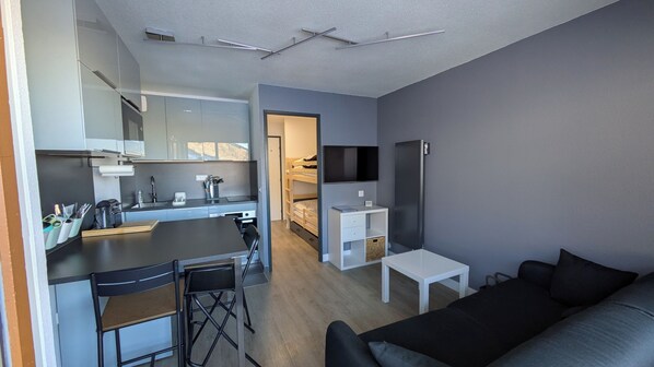 A modern apartment with a kitchen, dining area, and living room. It includes a sofa, a TV, and a small table.