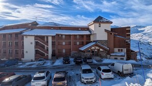 A large building with multiple floors, a prominent tower, and a parking lot filled with cars. - Mountain apartment Les Ménuires (Les Belleville)