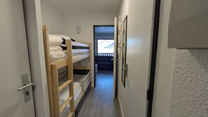 A narrow hallway with bunk beds on one side and a door leading to a balcony with a view of a mountainous landscape. - Mountain apartment Les Ménuires (Les Belleville)