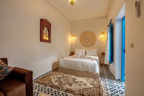 A hotel room with a bed, a chair, a decorative mirror, wall sconces, and a patterned rug. - Riad Les Secrets De Marrakech (Marrakech)