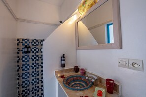 A bathroom with a geometric patterned wall, a sink with a decorative plate, a mirror, and a wall-mounted light fixture. - Riad Les Secrets De Marrakech (Marrakech)