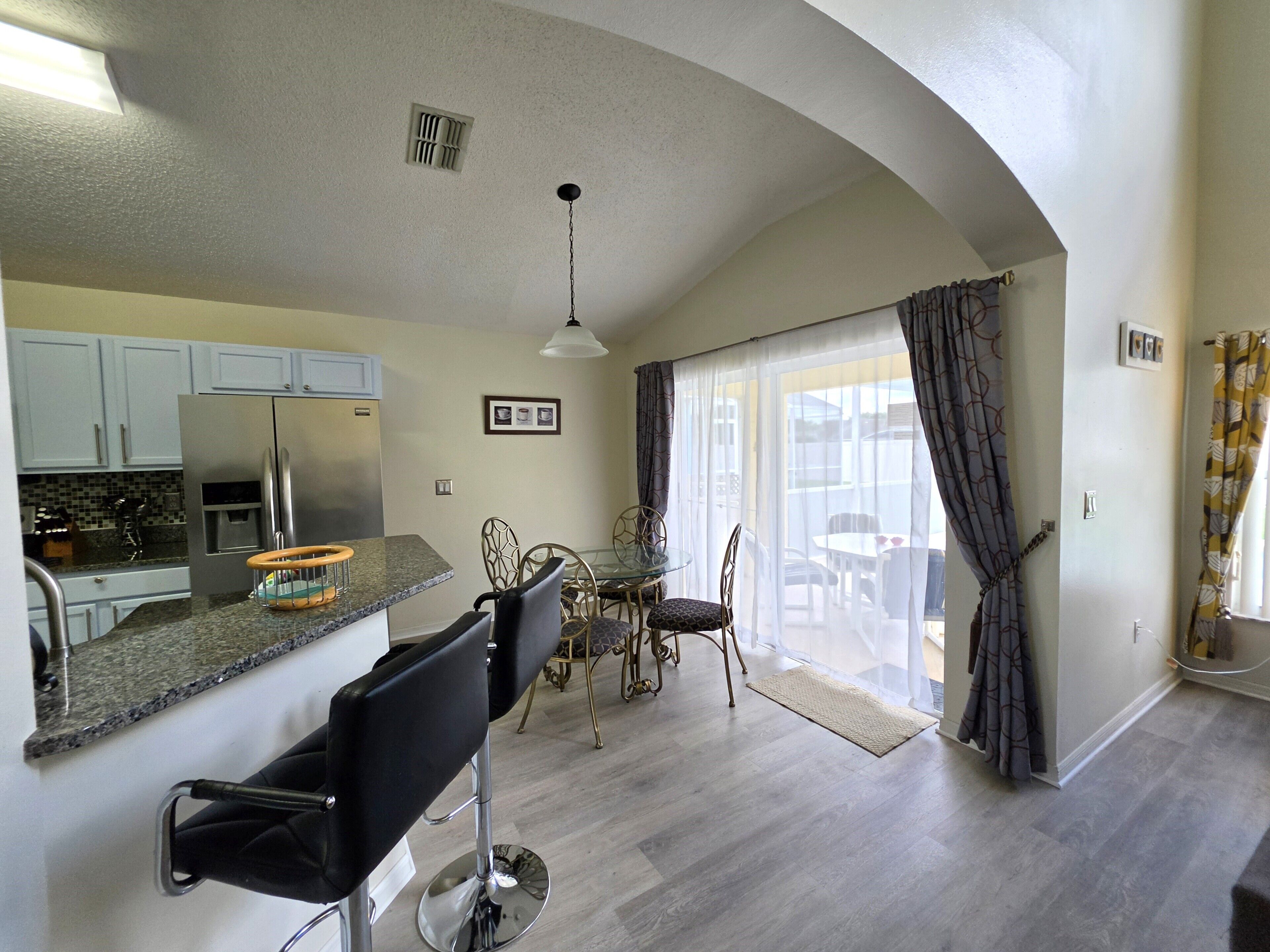 A modern kitchen with a built-in refrigerator, a dining area with a glass table and chairs, and a large sliding glass door leading to a patio.