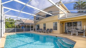 Un área de piscina con cerramiento de vidrio, sillas de descanso y un patio con mobiliario exterior.
