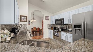 Una cocina con encimeras de granito, electrodomésticos de acero inoxidable y armarios blancos.