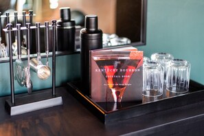 Ein Cocktailbuch mit dem Titel 'The Kentucky Bourbon Cocktail Book' von Joy Perrine und Susan Reigler, platziert auf einem Tablett zusammen mit Cocktailgläsern und einem Martini-Glas.