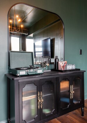 A black cabinet with a record player, a mirror, and a bottle of whiskey. - Hollyhock Suite 402: 4 bed/2 bath with soaking tub (Louisville)