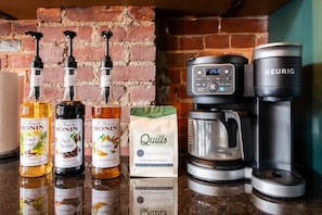 A kitchen counter with a coffee maker, a Keurig, and three bottles of Monin syrup. - Hollyhock Suite 402: 4 bed/2 bath with soaking tub (Louisville)