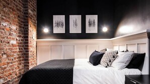Camera da letto moderna con parete in mattoni, una testiera bianca e tre quadri appesi sopra il letto.