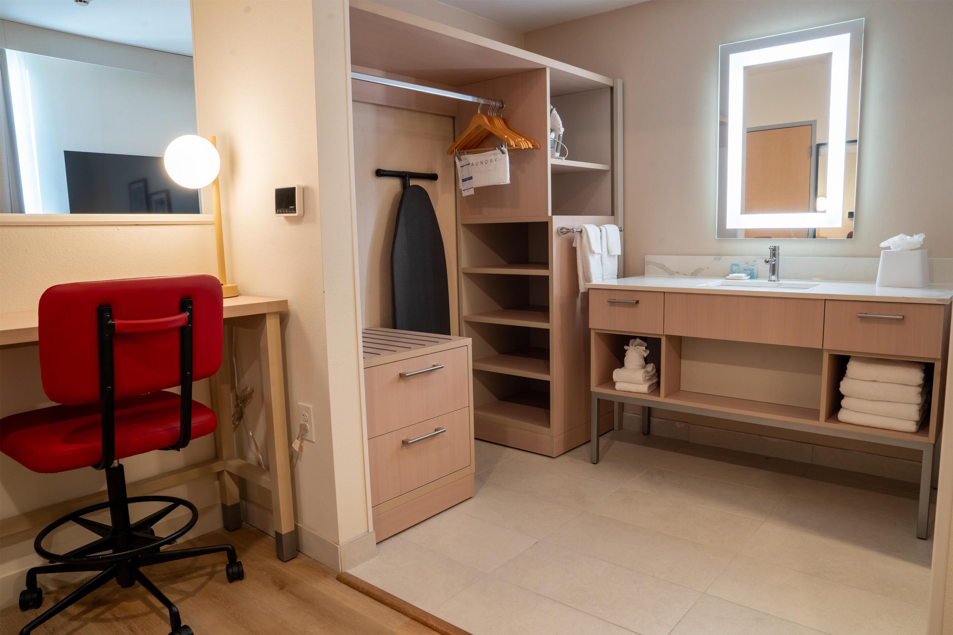 Un dormitorio pequeño con una silla roja, un armario, un espejo y una mesita de noche.