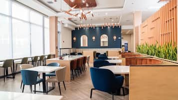 Un restaurant moderne avec un intérieur élégant, caractérisé par de hauts plafonds, un éclairage suspendu et une variété d’aménagements, notamment des tables et des banquettes.